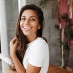 Claire closeup-portrait-pretty-woman-snow-white-t-shirt-posing-gray-room-with-wooden-furniture-min