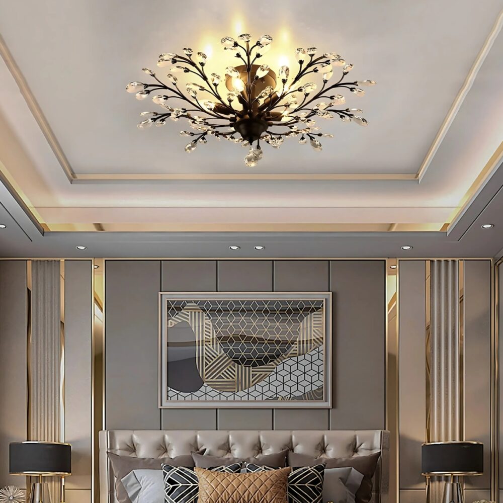 Lampe plafonnier avec branches noires et cristal fixé dans une chambre. Les ampoules dissimulées derrière les bourgeons de cristal diffusent une lumière jaune. Le plafond est blanc, les murs gris et beige avec un grand cadre sur le mur d'en face.