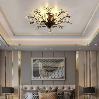 Lampe plafonnier avec branches noires et cristal fixé dans une chambre. Les ampoules dissimulées derrière les bourgeons de cristal diffusent une lumière jaune. Le plafond est blanc, les murs gris et beige avec un grand cadre sur le mur d'en face.