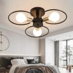 Lustre plafonnier avec 3 cercles noirs et une ampoule allumée dans chaque cercle. Fixé dans une chambre avec un lit double et une baie vitrée sur la droite.