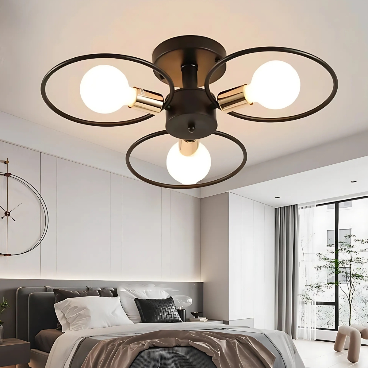 Lustre plafonnier avec 3 cercles noirs et une ampoule allumรฉe dans chaque cercle. Fixรฉ dans une chambre avec un lit double et une baie vitrรฉe sur la droite.