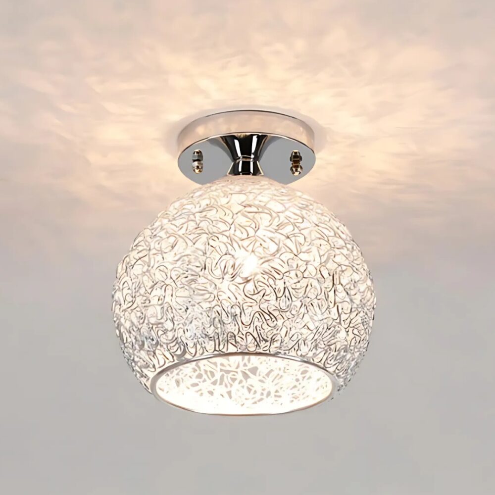 Lustre plafonnier boule en fil métallique argenté. L'ampoule au centre est allumée et elle diffuse un jeu de lumière au plafond.