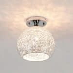 Lustre plafonnier boule en fil métallique argenté. L'ampoule au centre est allumée et elle diffuse un jeu de lumière au plafond.