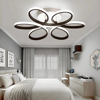 Plafonnier design en forme de boucles de couleur noire avec une bande LED tout le long des boucles Fixé dans une chambre aux murs gris avec un lit double et une literie blanche. En fond, une fenêtre aux voilages gris.