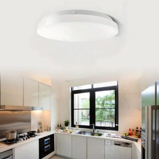 Plafonnier détecteur de mouvement circulaire à LED de couleur blanche dans une cuisine aux meubles blancs. Une fenêtre avec un encadrement noir en face avec l'évier en dessous.