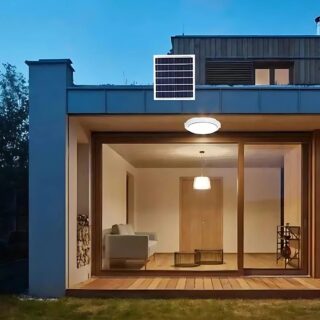 Plafonnier extérieur blanc solaire fixé sur le plafond d'une terrasse de maison. Le panneau solaire est fixé sur le haut du toit. On voit un salon à travers la baie vitrée.