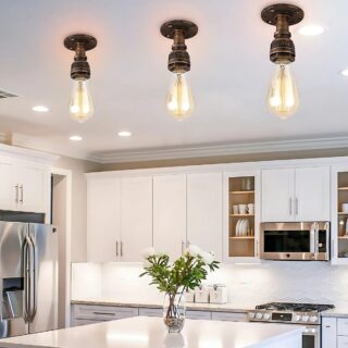 Plafonnier industriel minimaliste style tuyauterie vintage de couleur marron bronze. Trois plafonniers identiques sont fixés sur le plafond d'une cuisine avec un comptoir blanc brillant avec un vase et des fleurs. Des placards blancs sont accrochés au mur.