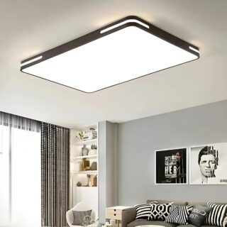 Plafonnier saloon avec éclairage LED de forme rectangulaire aux contours noirs. L'ensemble du rectangle est un diffuseur de lumière. Fixé dans un salon avec un mur gris sur la droite et deux cadres au-dessus d'un canapé. Sur la gauche une grande baie vitrée avec des rideaux marrons.