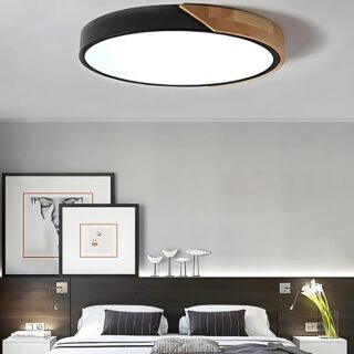 Plafonnier sans fil au design moderne noir et imitation bois de forme ronde. La lumière est allumée. Il est fixé au-dessus d'un lit double. Le mur en tête de lit est gris et le bas noir.