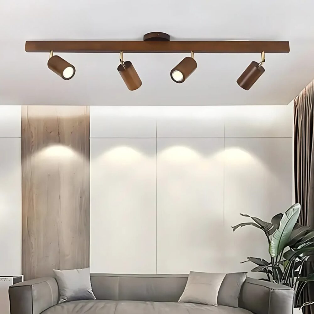 Plafonnier spots orientables en bois de couleur marron foncé avec 4 têtes allumées. En-dessous un canapé gris avec une plante verte sur la droite.