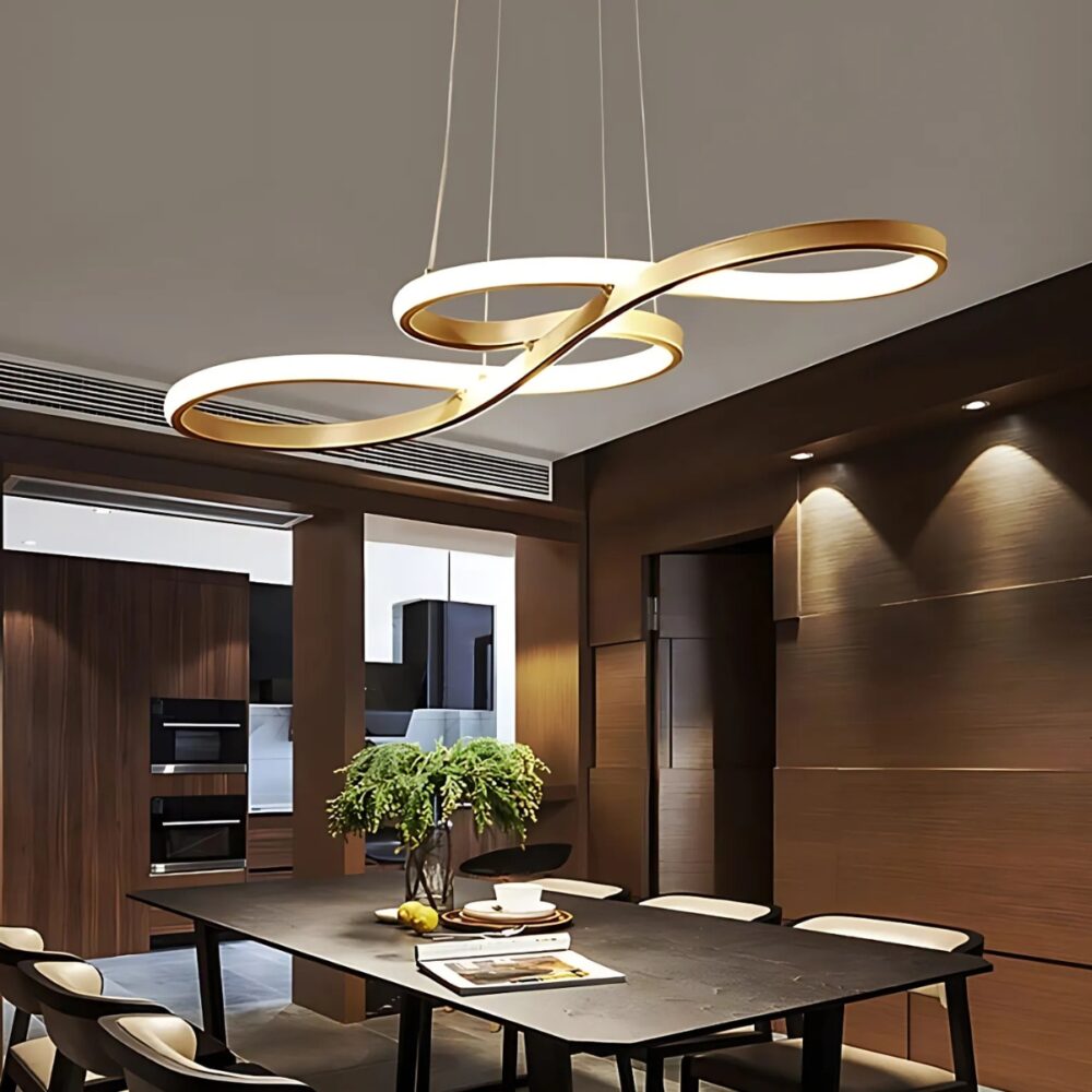 Plafonnier suspendu aux courbes fluides - Blancโ Plafonnier suspendu aux courbes fluides de couleur dorรฉe avec la bande lumineuse sur l'ensemble des courbes. Il est fixรฉ au-dessus d'une table rectangulaire en bois avec des chaises autour. Les murs de la piรจces sont marron.