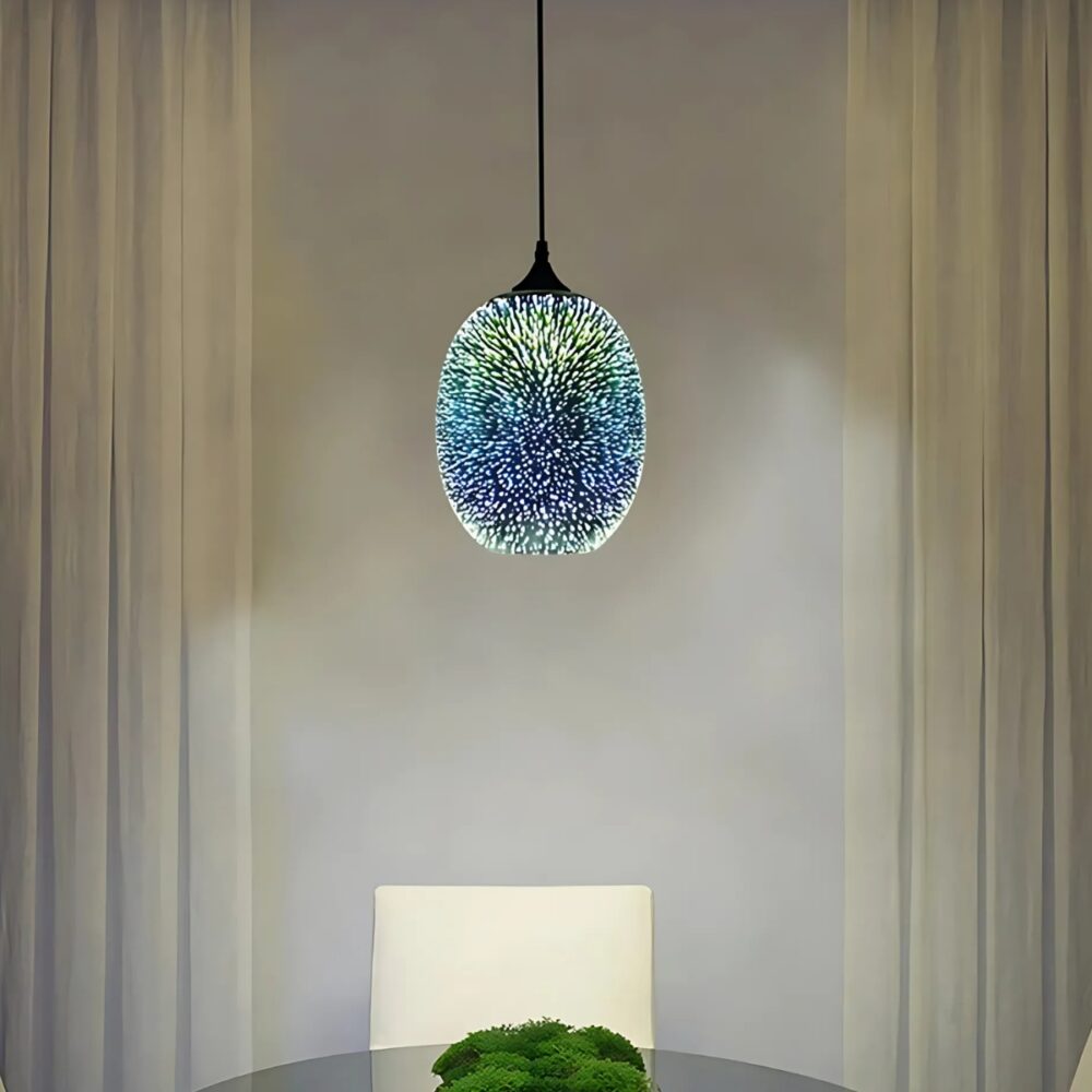 Plafonnier suspendu boule en verre avec un effet 3D de couleur bleu comme un motif de feu d'artifice. Allumé et suspendu au-dessus d'une table ronde avec une chaise blanche.