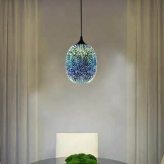 Plafonnier suspendu boule en verre avec un effet 3D de couleur bleu comme un motif de feu d'artifice. Allumé et suspendu au-dessus d'une table ronde avec une chaise blanche.