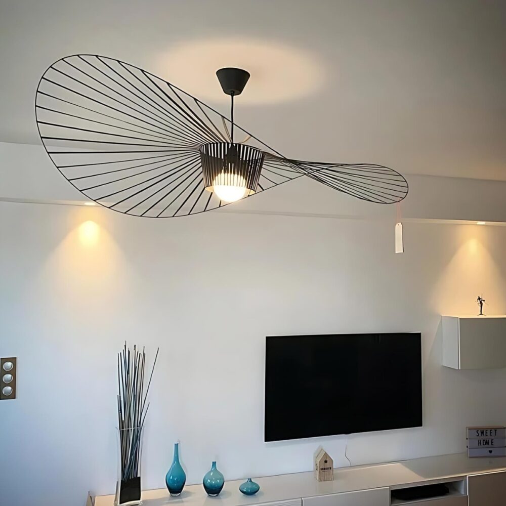 Plafonnier suspendu style vertigo de couleur noir avec une forme de chapeau capeline. L'ampoule est allumée. Il est fixé dans un salon ou on voit un écran noir au mur.