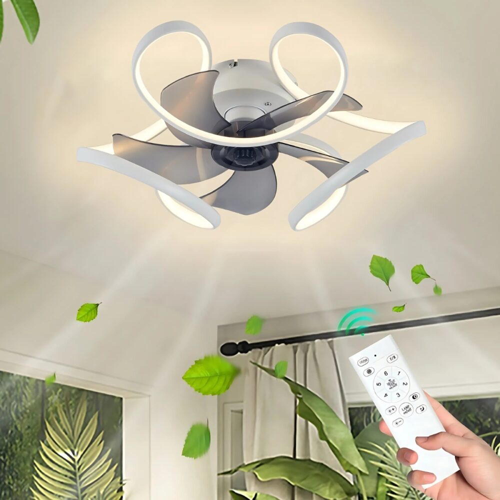 Plafonnier ventilateur élégant et compact avec des pales gris transparentes et un contour ondulé lumineux et blanc. En bas à droite, une main tenant une télécommande blanche. On voit des plantes vertes autour et un mouvement de vent sous le ventilateur.