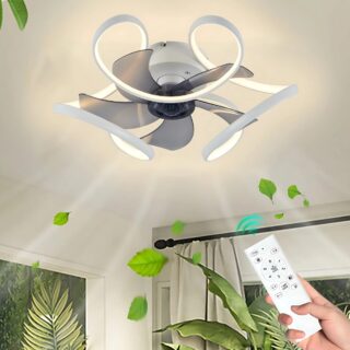 Plafonnier ventilateur élégant et compact avec des pales gris transparentes et un contour ondulé lumineux et blanc. En bas à droite, une main tenant une télécommande blanche. On voit des plantes vertes autour et un mouvement de vent sous le ventilateur.