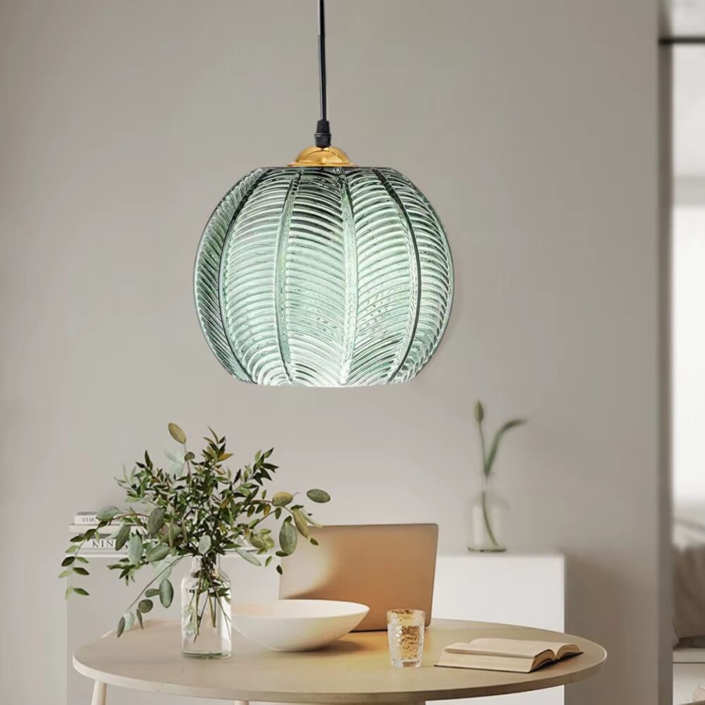 Suspension en verre nervuré vert foncé en forme de sphère avec reliefs, suspendue par câble noir et finition dorée au sommet.