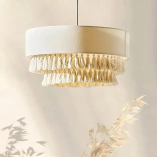 Suspension style bohème avec un abat jour beige en tissu et deux rangées de pompons qui pendent sur un fond neutre