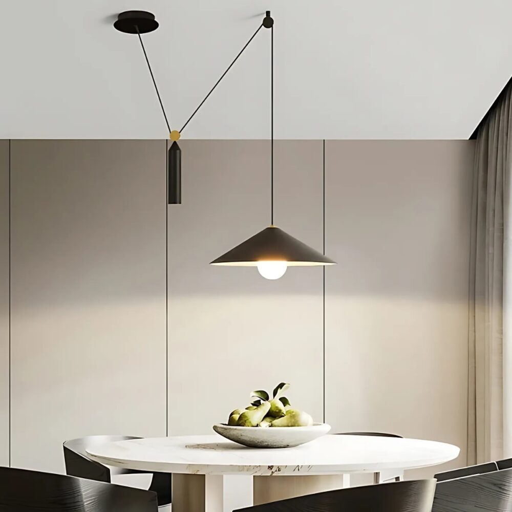 Plafonnier déporté avec hauteur ajustable de couleur noire. Son abat-jour est de forme conique, le câble est noir relié avec un point au plafond puis un balancier cylindrique noir. L'ampoule est allumée. Il est fixé au-dessus d'une table ovale beige avec des sièges noirs.