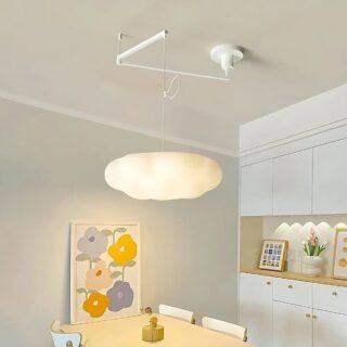 Plafonnier déporté en forme de nuage suspendu par deux bras en métal. Fixé au-dessus d'une table blanche avec des chaises assorties. Sur la droite un meuble blanc avec tiroirs et portes et des décorations.