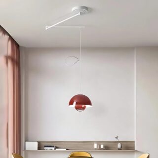 Plafonnier déporté moderne coloré avec un bras orientable en 2 parties. L'abat-jour rond est de couleur rouge avec la lumière reflété à l'intérieur. Il est suspendu par un câble blanc relié aux bras pliables. Dans une pièce aux murs blancs avec une baie vitrée sur la gauche, une table ronde et des sièges jaunes sous le plafonnier.
