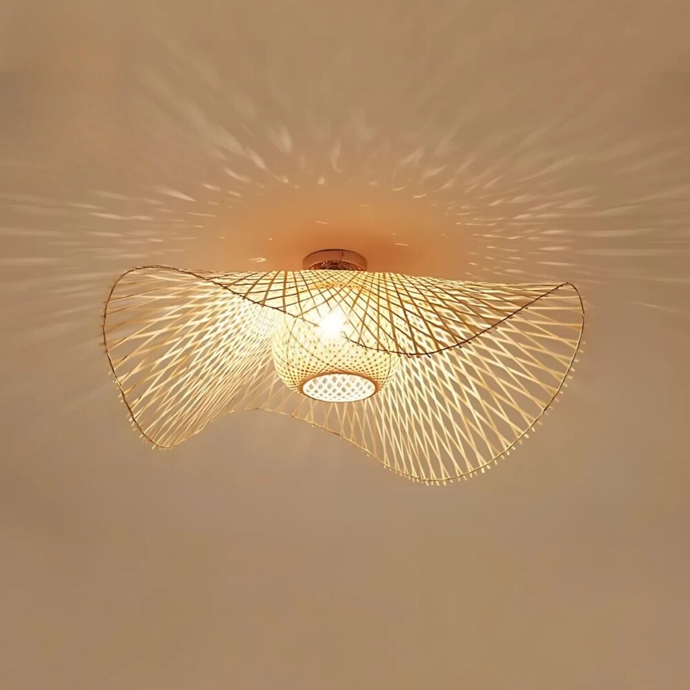 Plafonnier naturel en rotin style capeline avec une ampoule allumée diffusant une lumière à travers le tressage. Fixé sur un plafond beige.