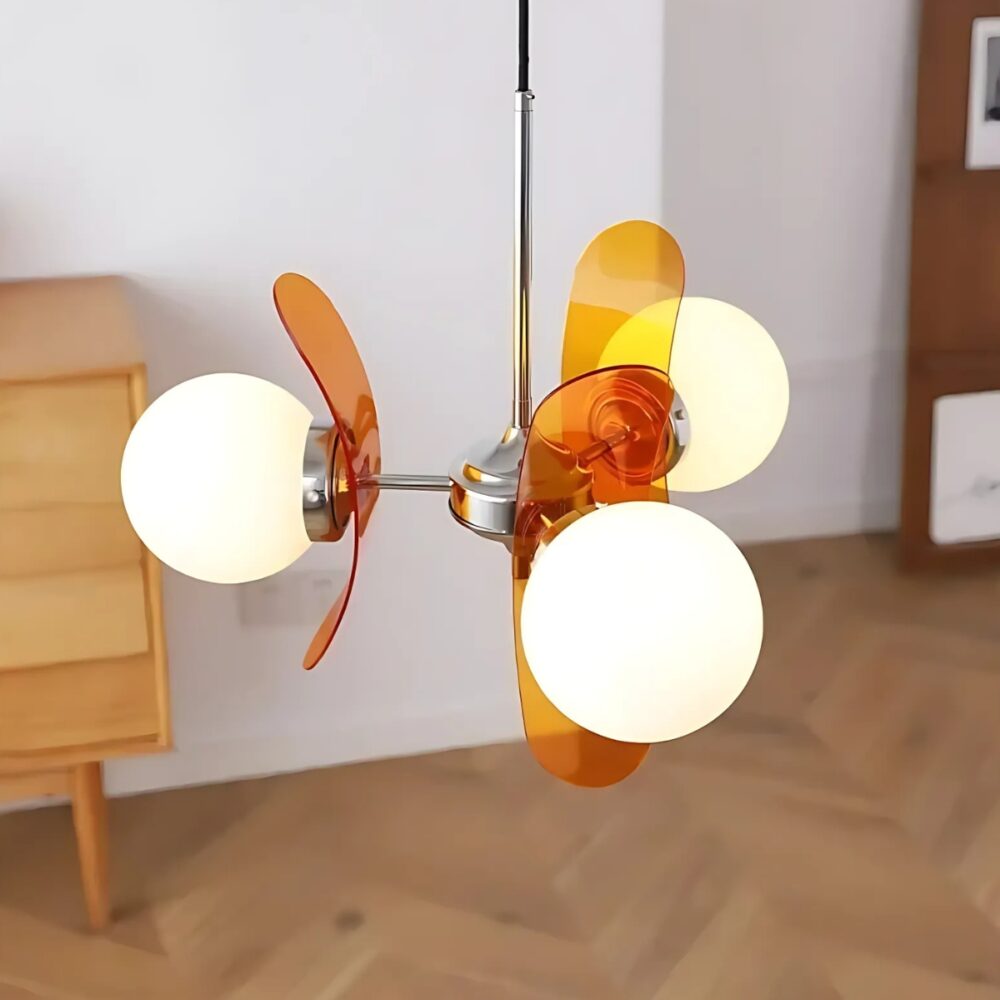 Luminaire plafonnier rétro coloré avec boules lumineuses Luminaire plafonnier rétro en verre avec boules lumineuses. Il est muni de trois plaques en verre orange et trois boules lumineuses allumées. Suspendu par une tige chromé, il se trouve dans une pièce avec un sol de type parquet flottant et une commode en bois.