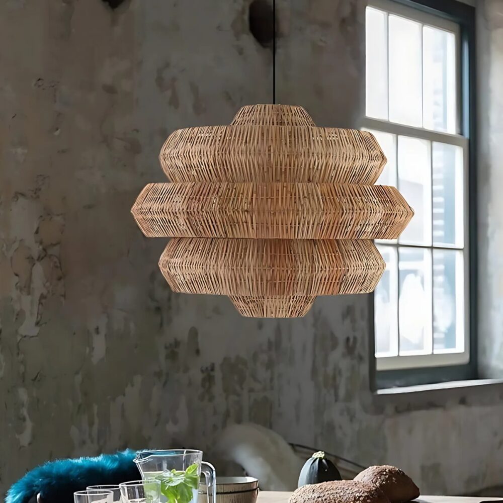 Lustre plafonnier en rotin naturel suspendu dans une pièce aux murs gris style béton. Sous le lustre, une table et sur la droite une fenêtre.