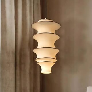 Lustre plafonnier vertical en tissu formant un tube avec plusieurs anneaux en métal. Suspendu et allumé dans une pièce avec un mur marron et un rideau beige sur la gauche.