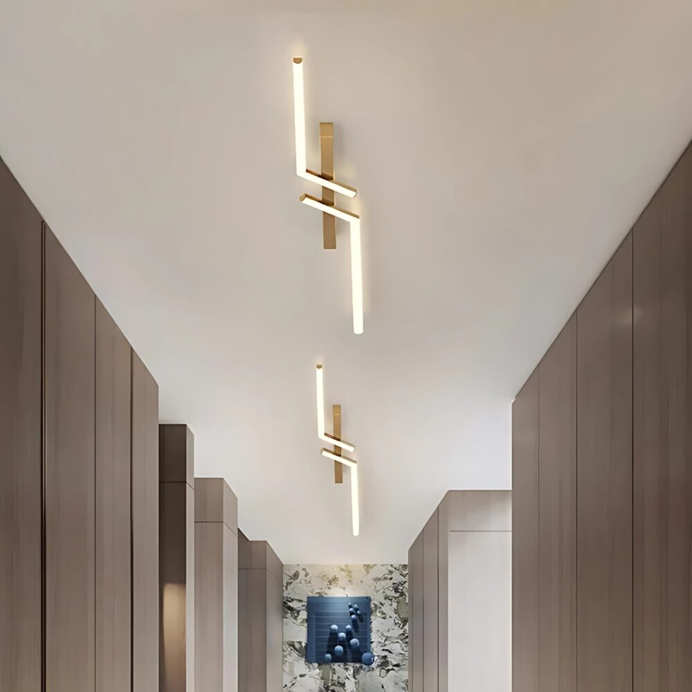 Plafonnier moderne en LED style industriel en forme de double L, de couleur doré sur un fond beige situé dans un dressing avec un tableau bleu au fond du couloir