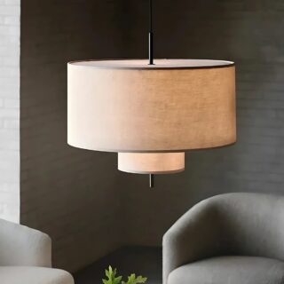 Plafonnier japonais suspendu en tissu avec deux niveaux : un grand cercle et un plus petit en dessous. L'éclairage est jaune. On voit deux fauteuils gris et un mur gris au fond.