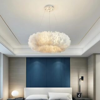 Plafonnier suspendu en forme d'anneau de plumes blanches. Trois câbles fins tiennent l'anneau de plumes. Une lumière jaune est diffusée au centre. Fixé dans une chambre avec un lit double blanc, un mur bleu canard en tête de lit et le reste des murs sont beiges.