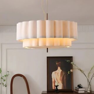 Plafonnier suspendu en tissu ondulé de couleur beige. L'éclairage est jaune. Le plafonnier est fixé dans une pièce avec en fond un tableau, un meuble et un miroir.
