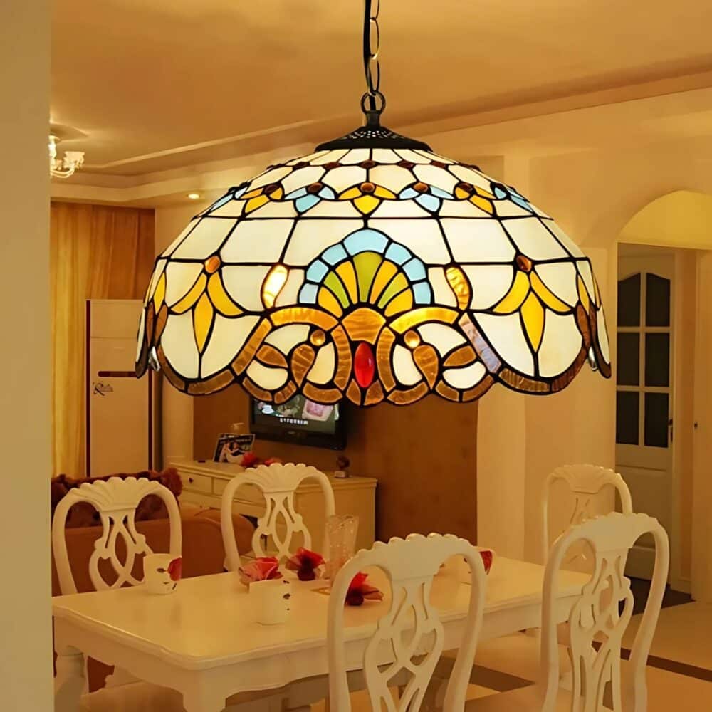 Plafonnier Tiffany suspendu jaune en verre. L'ampoule est allumée et diffuse une lumière jaune. On voit une table rectangulaire blanche avec 5 chaises blanches autour de celle-ci.