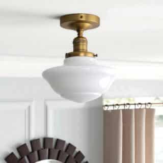 Plafonnier vintage doré et verre blanc en forme de demi cercle. Fixé sur un plafond blanc avec en fond un rideau beige et un cadre rond en bois.