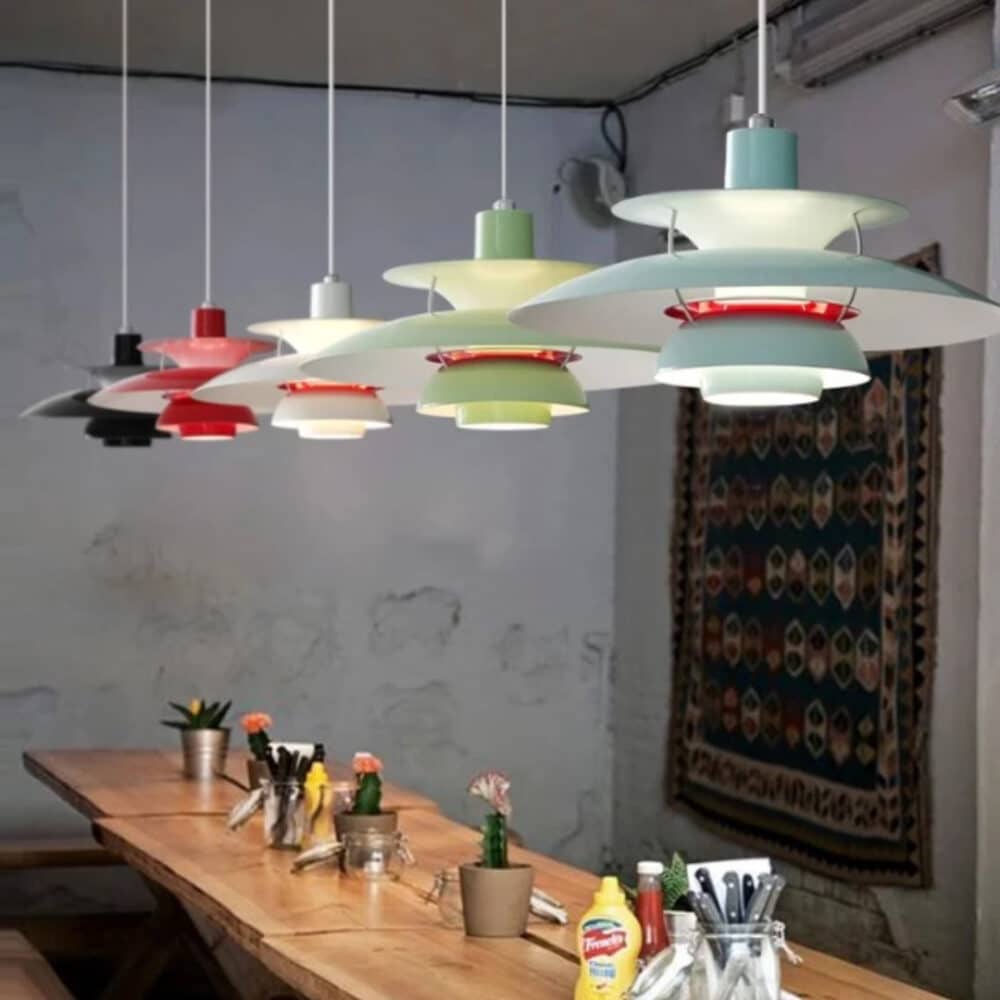 Une suspension rétro nordique à diffuseurs superposésticouches illumine au-dessus d’une grande table en bois dans une salle au mur gris.